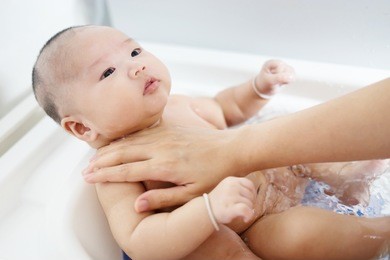 baby bath time concept,portrait of a baby is being bathed by his mother using tub at home,selective focus