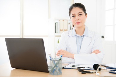 confident female doctor sitting at office desk giving all patient convenience online service and smiling with hands crossed, health care and prevention disease concept.
