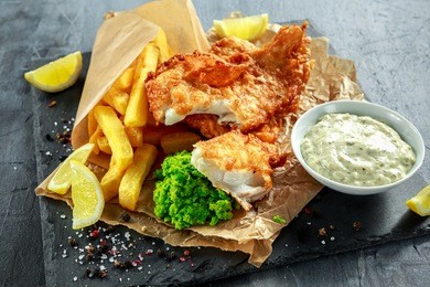 british traditional fish and chips with mashed peas, tartar sauce on crumpled paper.
