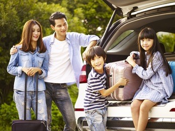 cute asian children helping unloading luggage from trunk while parents watching affectionately.