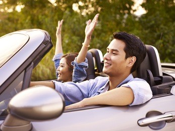 young asian couple riding in a convertible sport car at sunset.