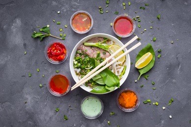 traditional vietnamese noodle soup pho in bowl, garnished with basil, mint, lime, on concrete background
