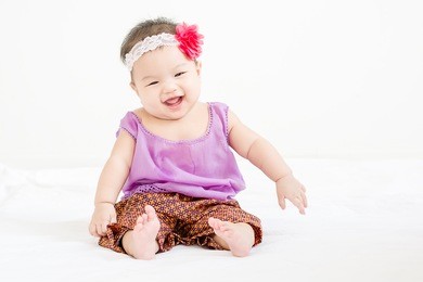portrait of a little adorable infant baby girl sitting on the bed and smiling to camera with copyspace