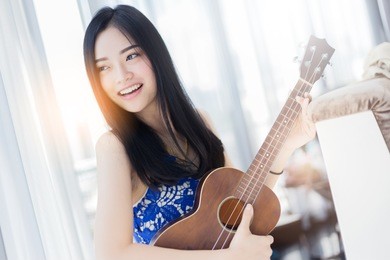 beautiful asian woman playing ukulele with happiness and joyful near widow white room background