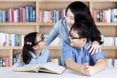 image of two cute students talking and studying with their teacher while sitting in the library