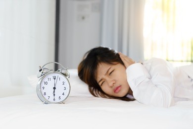 sleepy young woman looking at alarm clock with hands covering her ears in the morning. early wake up