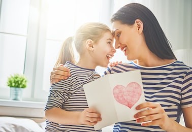 happy mother's day! child daughter congratulates mom and gives her postcard. mum and girl smiling and hugging. family holiday and togetherness.