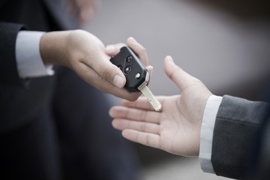 car salesman handing over the keys for a new car to a young businessman