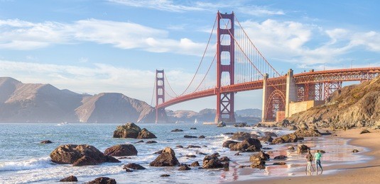 classic panoramic view of famous golden gate bridge seen from scenic baker beach in beautiful golden evening light on a sunny day with blue sky and clouds in summer, san francisco, california, usa