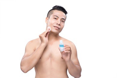 confident man applying lotion after shave on face over white background.