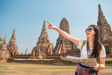 travel tourist woman holding map in wai chaiwatthanaram, ayutthaya and looking and pointing for copyspace traveling in asia smiling happy having fun in thailand.