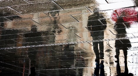 blurry reflection silhouette of a woman and a man walking in the rain in the city pebbled sidewalk