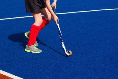 a girl playing field hockey on blue "wet" turf