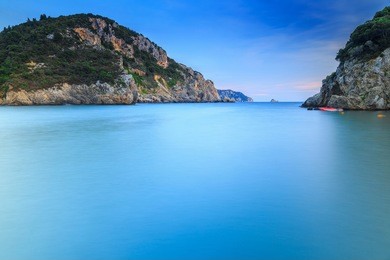 long exposure landscape of paleokastritsa famous sand beach in close bay on corfu island at dusk. focus at foreground. ionian archipelago, greece.