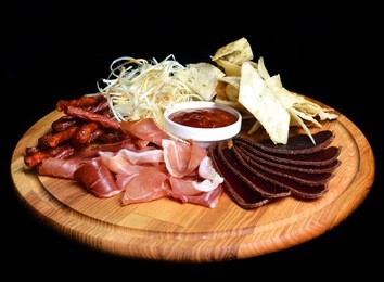 snack to beer on a wooden board. basturma, dried meat, dried squid, chips isolated on a black background.