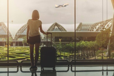 silhouette of the young female tourist with a bag standing near the window at the airport and looking at the garden outside while waiting for check in. mock up, copy space for your text.