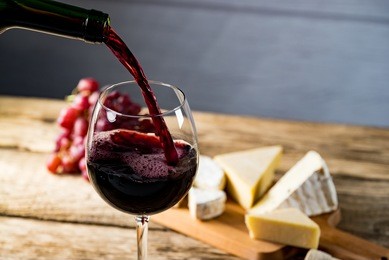 pouring red wine into the glass against wooden table