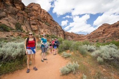 smiling group of hikers enjoying the day hiking together along a beautiful desert cliff hiking trail in utah. natural beautiful in a national recreation park. 