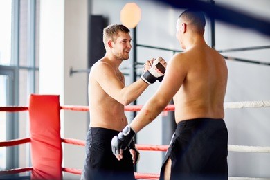 portrait of two opponents shaking hands and smiling after good fight in boxing ring during practice