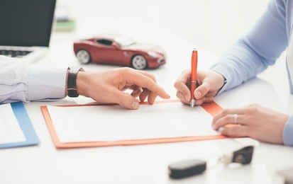 woman signing a car insurance policy, the agent is pointing at the document