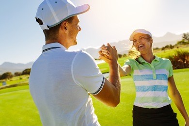 happy male and female friends shaking hands at golf course after the game. pro golfer enjoying the game on field.