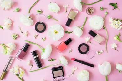 feminine desk with cosmetics, lipstick, nail polish, eye shadows and white flowers on pink background. flat lay, top view. beauty background