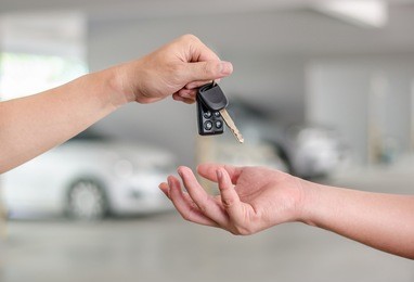 male hand holding a car key and handing it over to another person