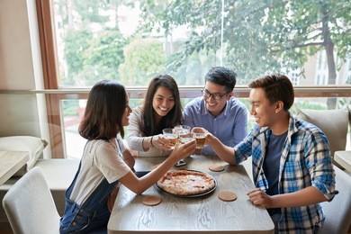 friends toasting before eating pizza in cafe