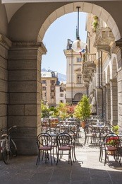 aosta, italy - august 7, 2010: in place (square) chanoux, the arcade of the city hall with chairs and tables of an outdoor cafe, and a bicycle.