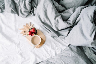 breakfast in bed with coffee mug and strawberry. bright grey linens. flat lay, top view.