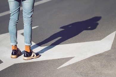 side view close up of a young woman wearing black shoes and blue jeans standing on a street with arrow signs pointing in different directions concept for life choices