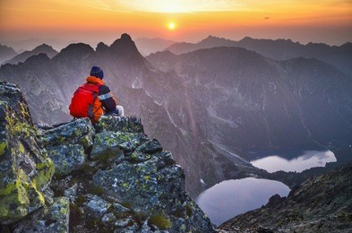 man on the top of mountain with beautiful scenery all around - summer sunset sky, rocks, valley and two lakes