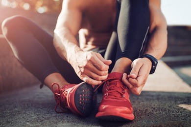 man tying jogging shoes.a person running outdoors on a sunny day.
