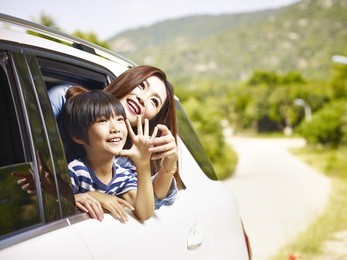 happy asian mother and son sticking heads out of rear window of a car looking at scenery.
