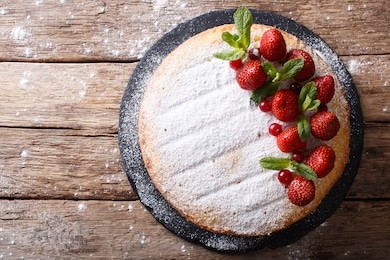 whole victoria sandwich cake, decorated with strawberries, cranberries and mint closeup on the table. horizontal view from above
