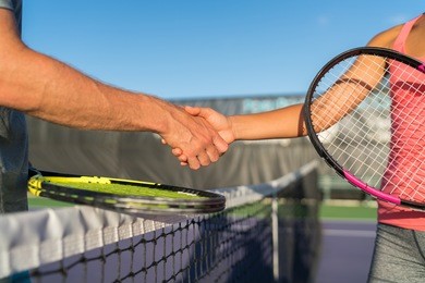 tennis players shaking hands at court net at end of fun game. man and woman playing recreational tennis handshaking with tennis racquets.