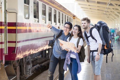 group of asian and caucasian man traveler are pointing and looking out with train station background. travel in summer concept.