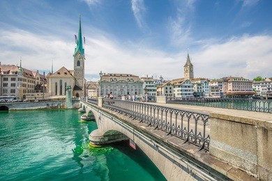 panorama view of historic city center of zurich with famous fraumunster church and munsterbucke crossing river limmat on a beautiful sunny day with blue sky and clouds, switzerland