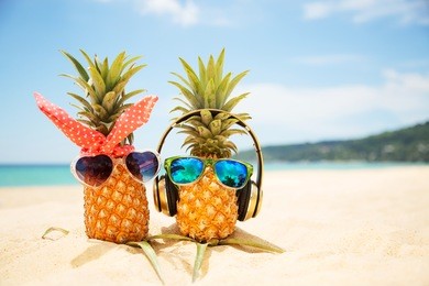 couple of attractive pineapples in love on the sand against turquoise sea. wearing stylish mirrored sunglasses. tropical summer vacation concept. sunny day on the beach of tropical island. honeymoon 