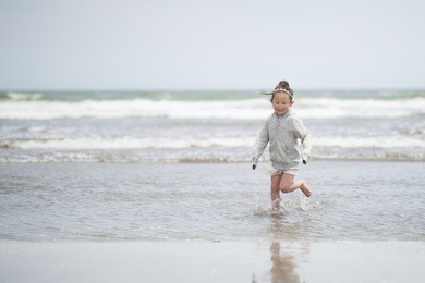 little girl in a parka playing on the beach