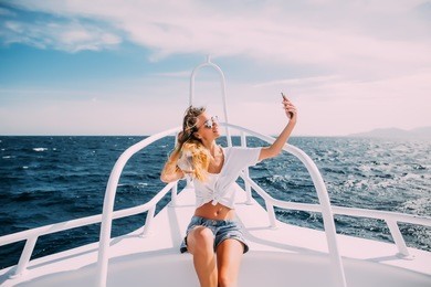 young beautiful brunette girl making selfie using phone while sitting on the luxury yacht