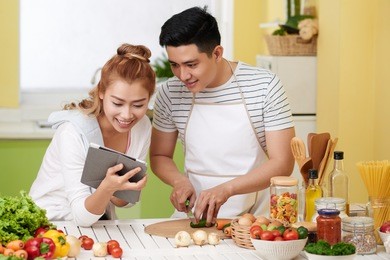 happy vietnamese couple following recipe on tablet computer when cooking