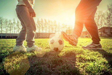 father and son playing together with ball in football under sun light. green field in city park at sunny day.