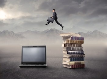 businessman jumping from some books to a laptop in a desert