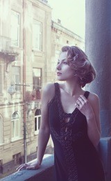 a beautiful slender girl in evening dress with blond hair of medium length stands leaning on the balcony. author's retouch in the violet light. shooting in daylight. soft focus, selective sharpness