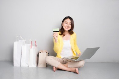 young asian woman shopping online at home sitting besides row of shopping bags