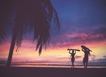 silhouette of surfer people carrying their surfboards on sunset beach, vintage filter effect