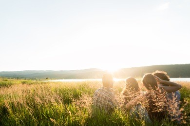 friends sitting together at lake in summer enjoying sundown and evening mood