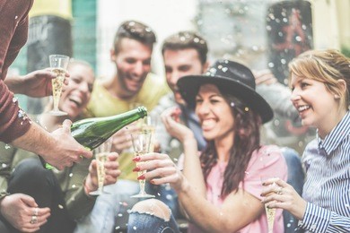 happy friends celebrating drinking champagne and making party outdoor - young loud people having fun outside - youth and fest concept - focus on left man hand with bottle - warm contrast filter