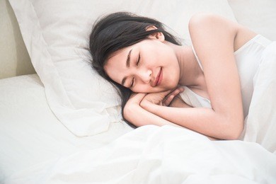 beautiful young asian woman with attractive smile laying on bed indoors. portrait of woman in bedroom